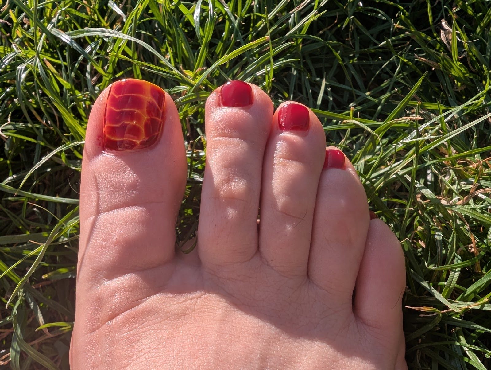 Bare feet on grass with a red pedicure and patterned accent toenails