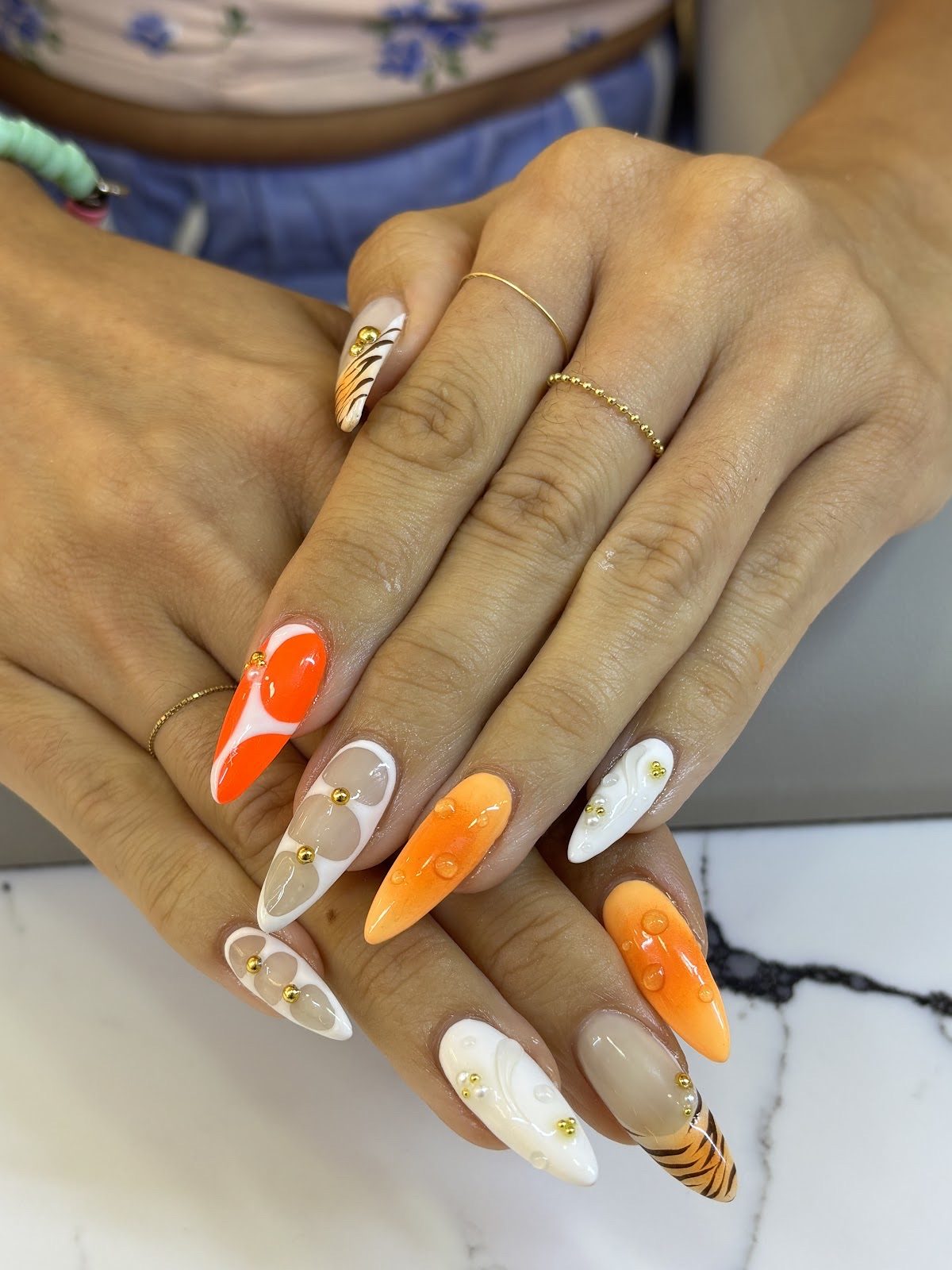 Two hands on a table showing almond nails in orange, white and gold marble art