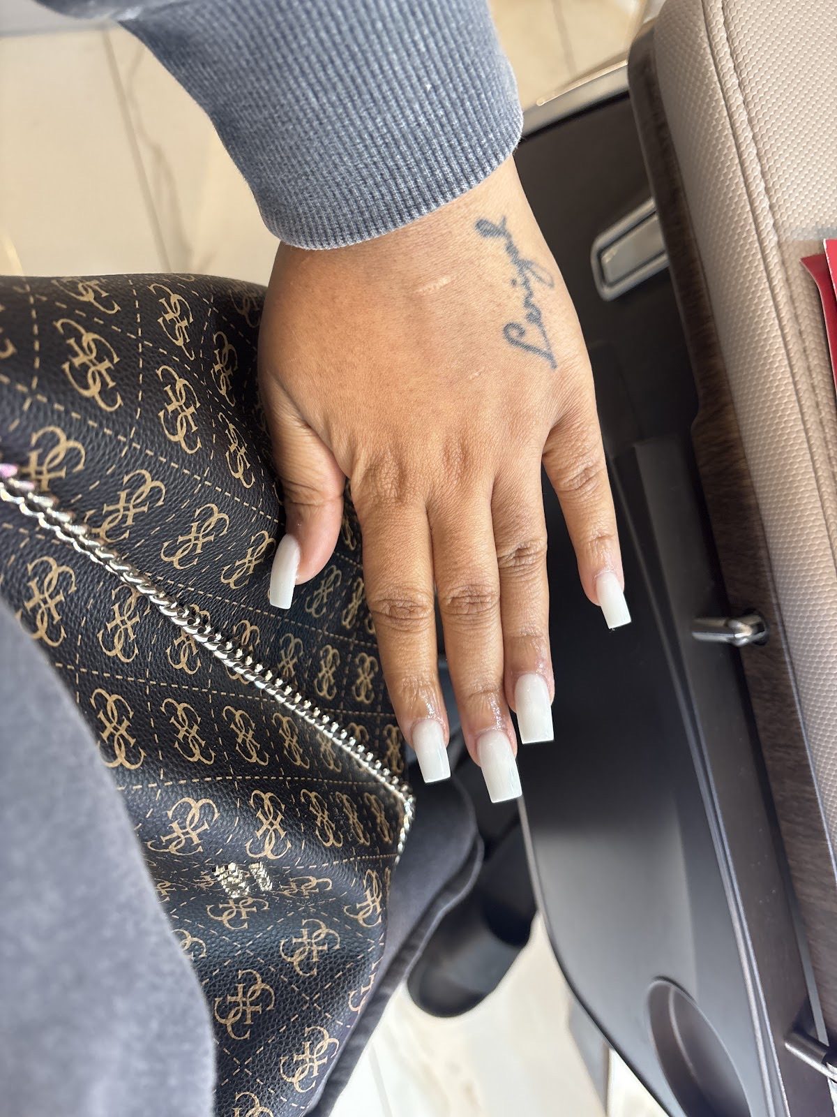 A hand with long square white-tip nails resting on a handbag